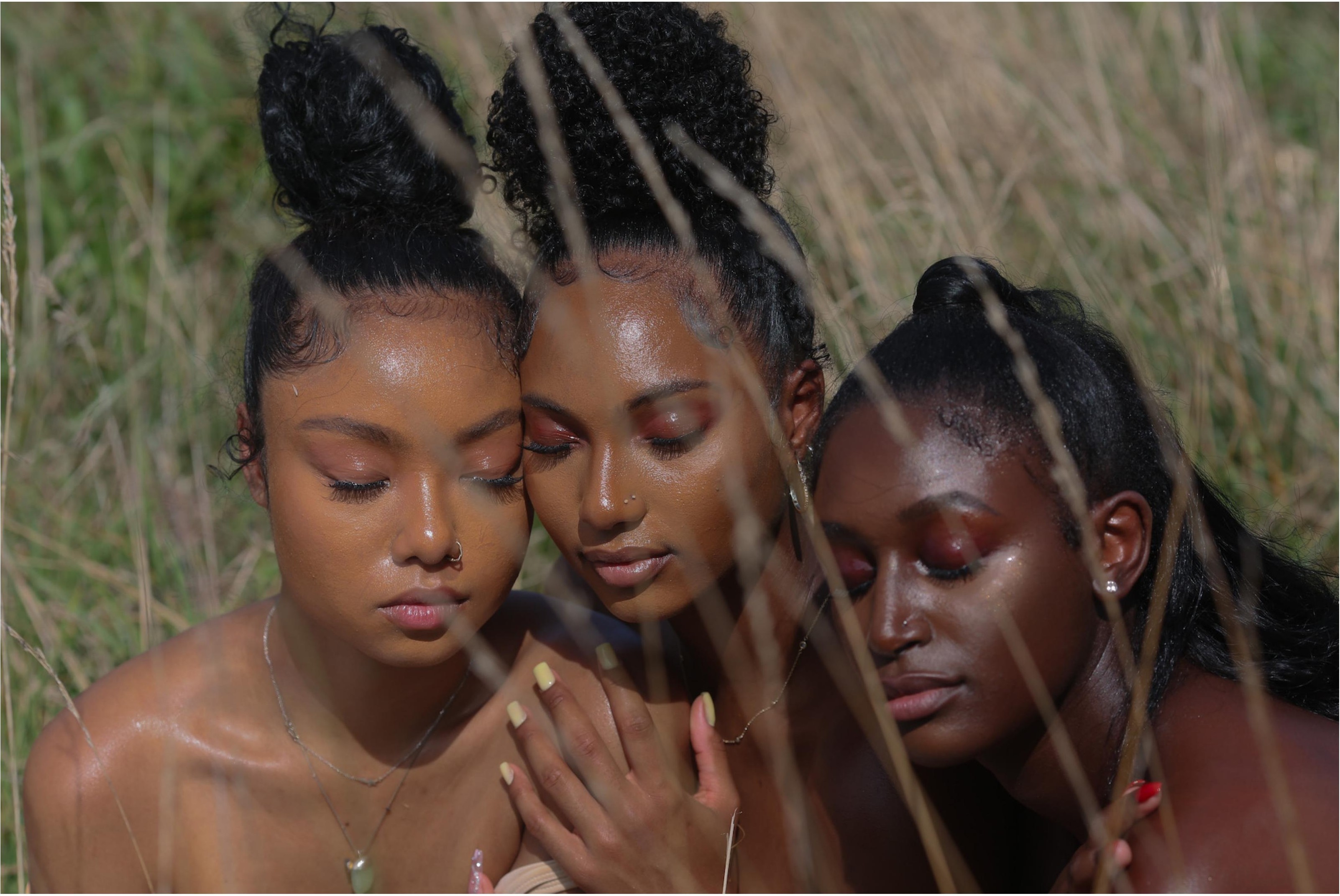 Three women with radiant, smooth skin resting together in tall sunlit grass